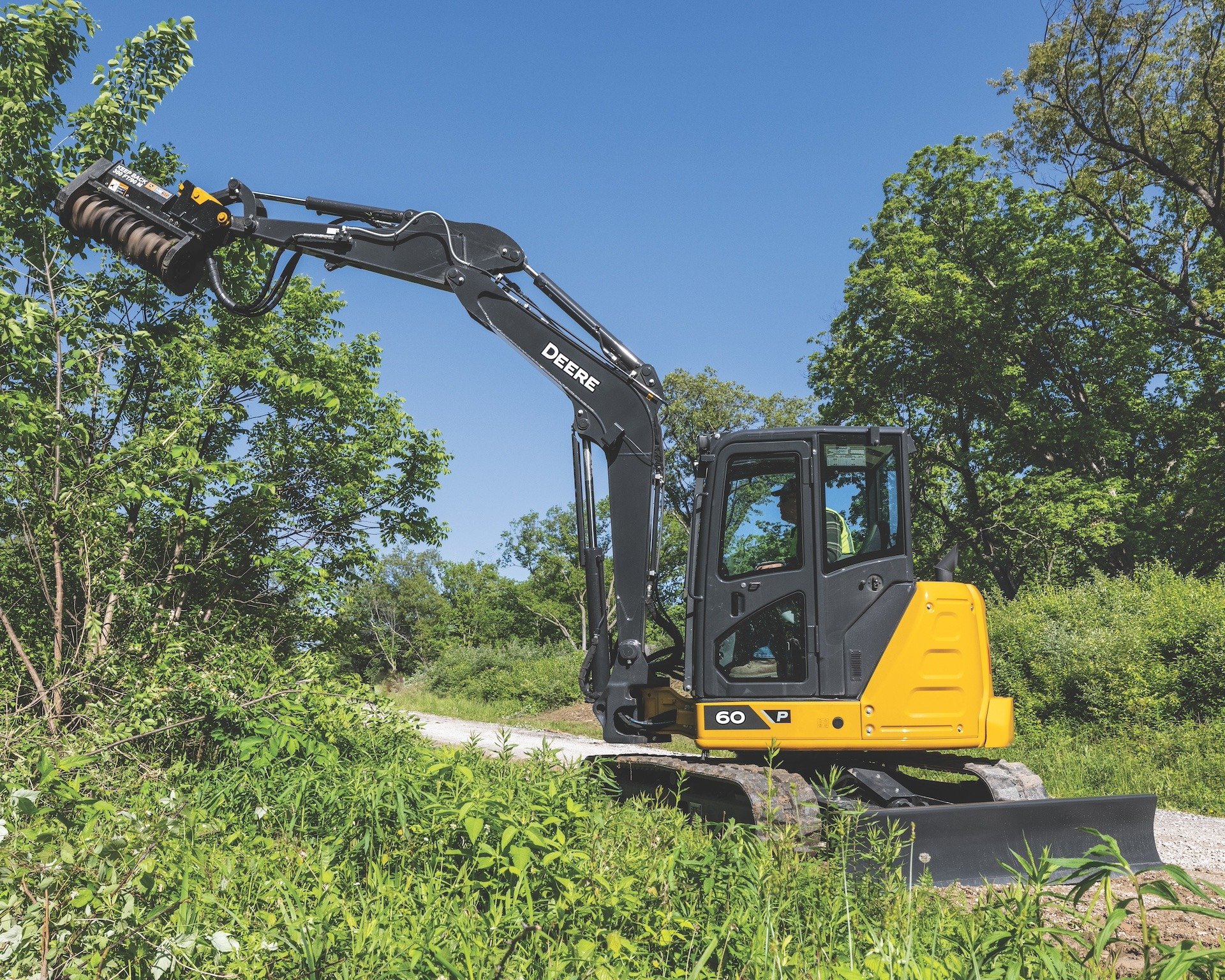 A John Deere 60 P-Tier compact excavator moving brush on a property.