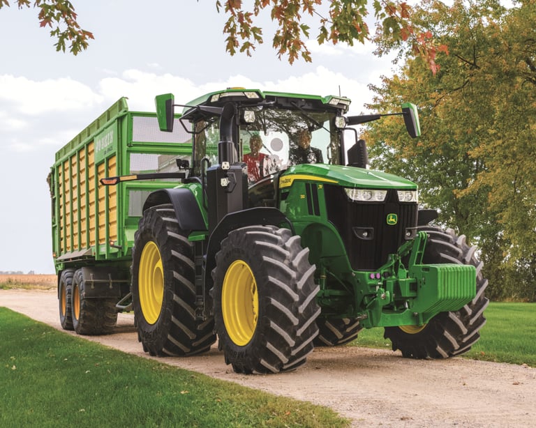 A farmer drives a John Deere 7R with a trailer attached.