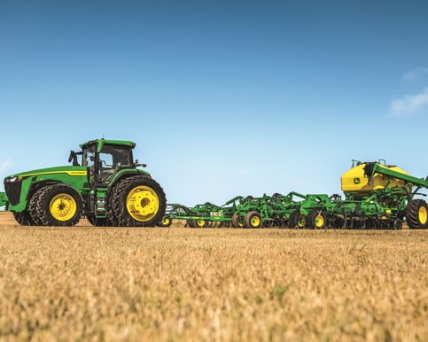 A John Deere 8R 410 tractor pulling an attachment and working in a field.