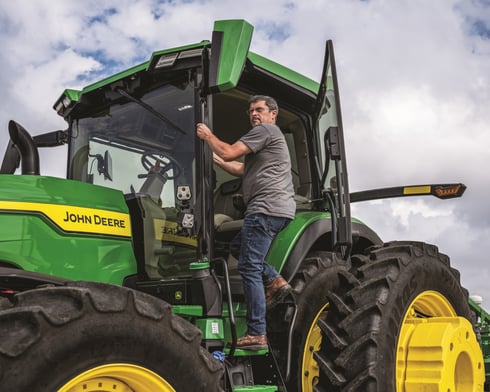 A worker enters the cab of a John Deere 8R 410 tractor.