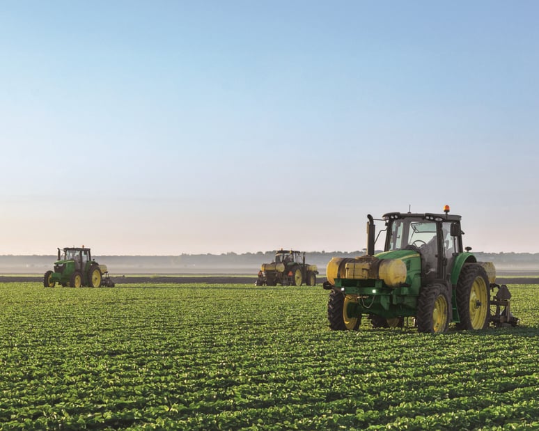 A fleet of John Deere tractors with sprayers navigate a field.
