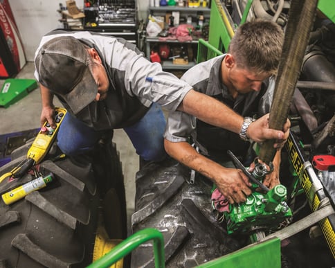 Two John Deere service technicians work on a John Deere machine.