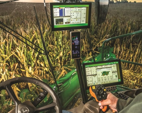 An operator commands a John Deere X91100 Combine with a monitor.