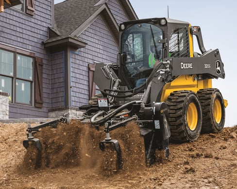 A John Deere skid steer prepares soil for construction.
