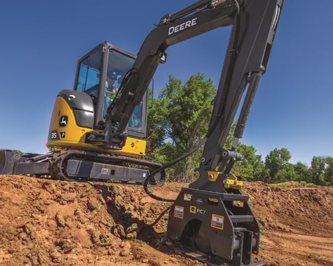 A John Deere compact excavator works the soil on a construction site.