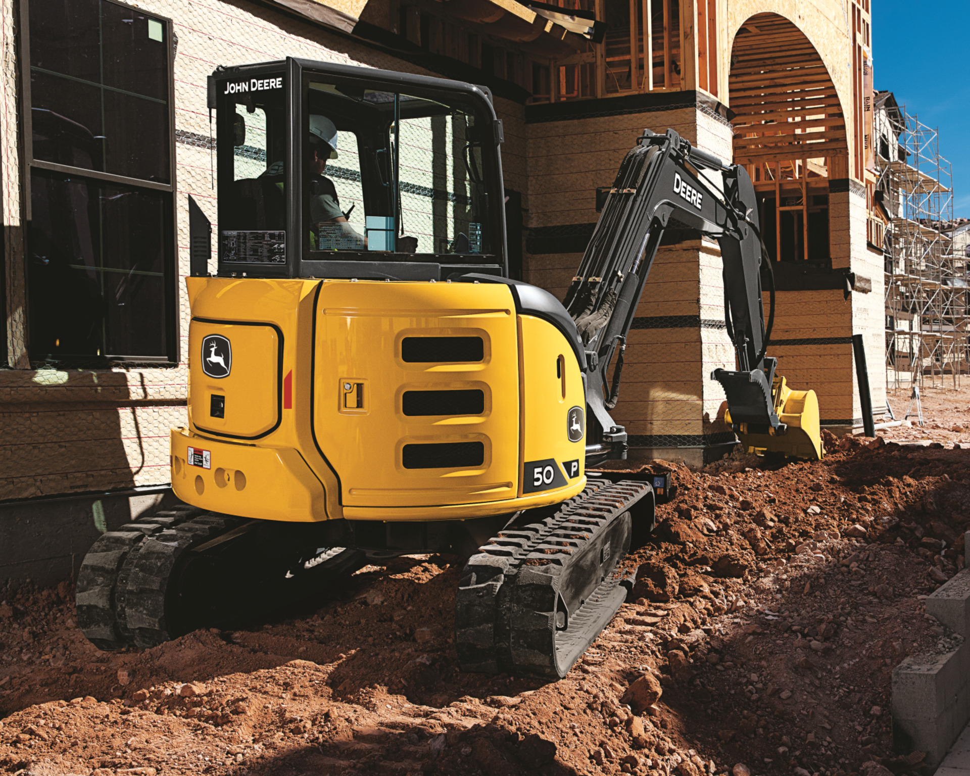 A John Deere 50P excavator fits in a tight space on a construction site.