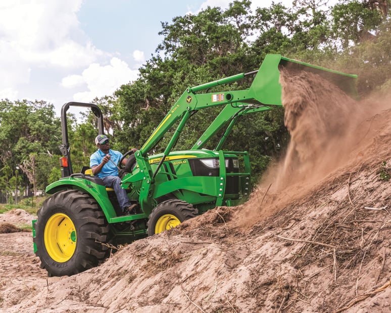 A man uses a front-end loader attachment to move dirt.