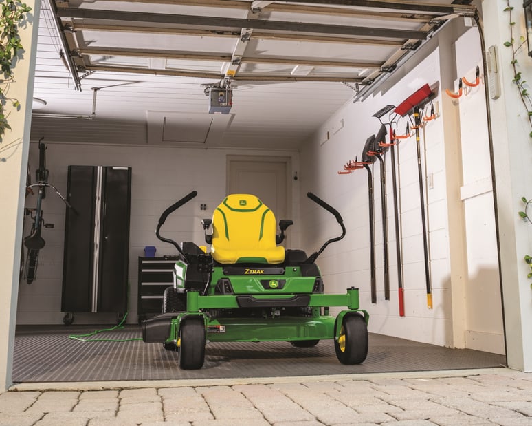 A John Deere ZTrak zero-turn electric mower sits in storage in a shed.