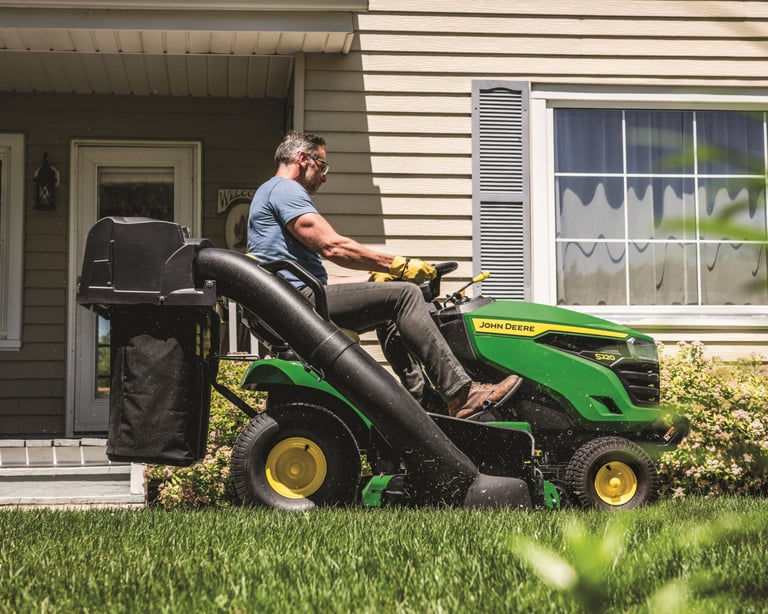 A man bags lawn clippings with a John Deere mower bagger attachment.