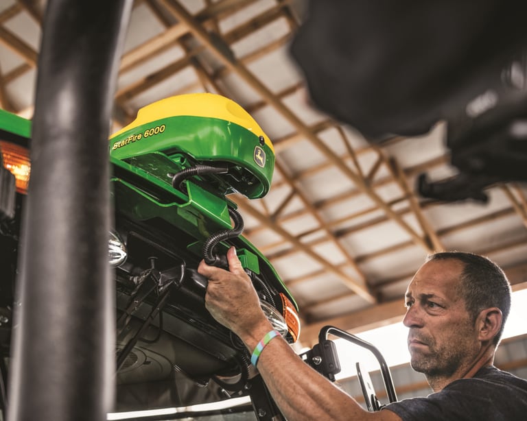A farmer inspects a StarFire Receiver on a John Deere tractor.