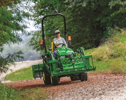 A woman operates a John Deere tractor.
