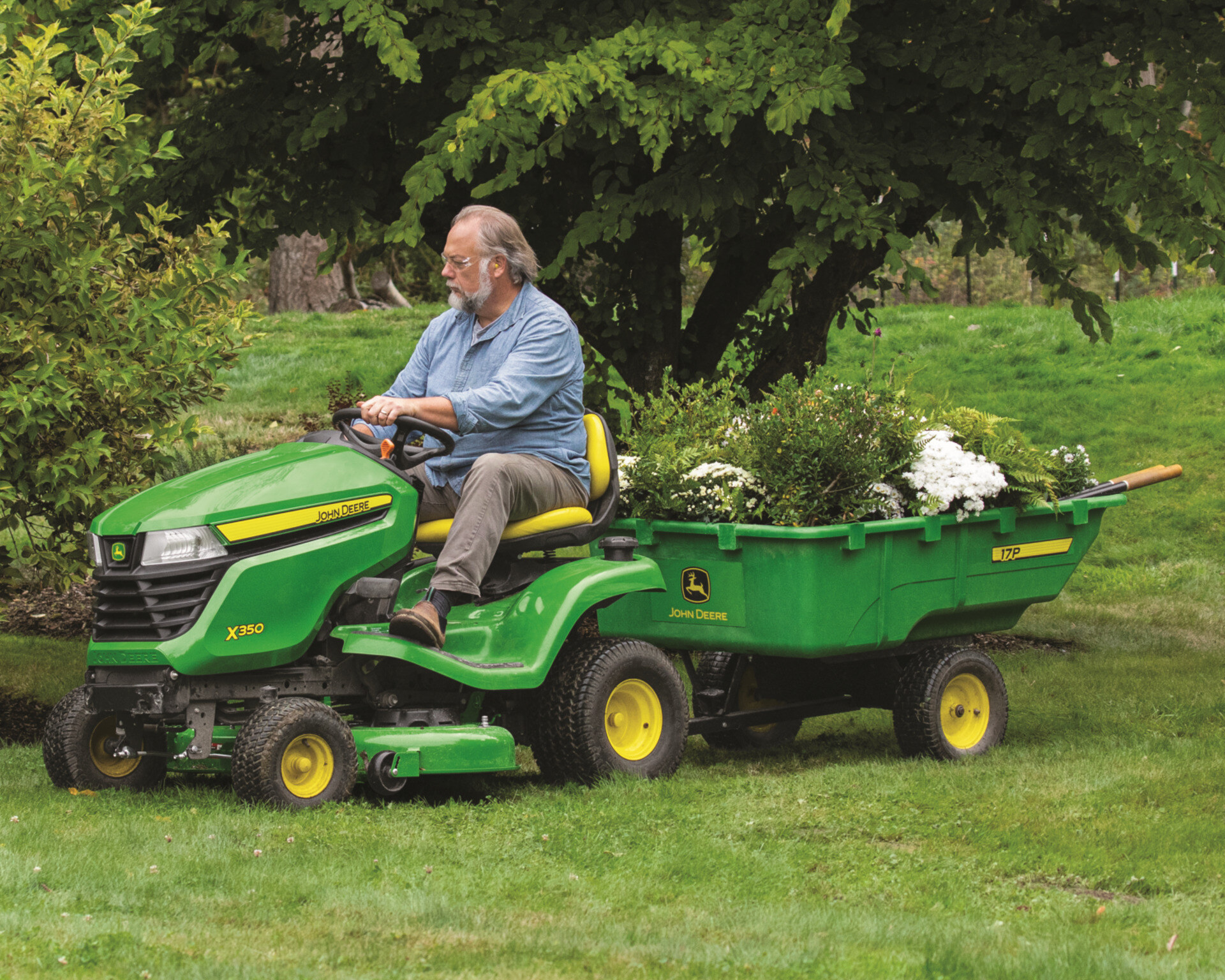 A John Deere X350 riding mower pulling a trailer with yard scraps.