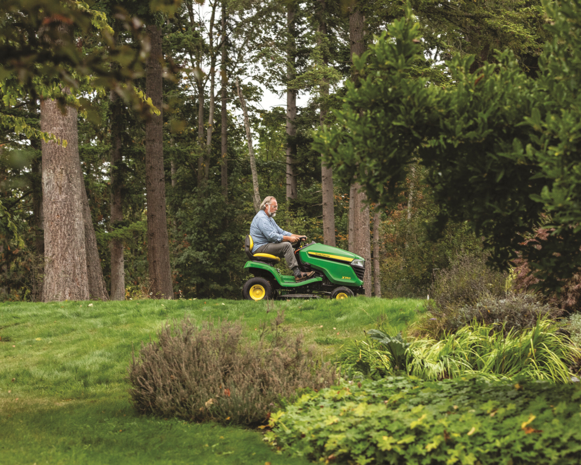 A man mows a lawn with a John Deere X350 riding lawn mower.