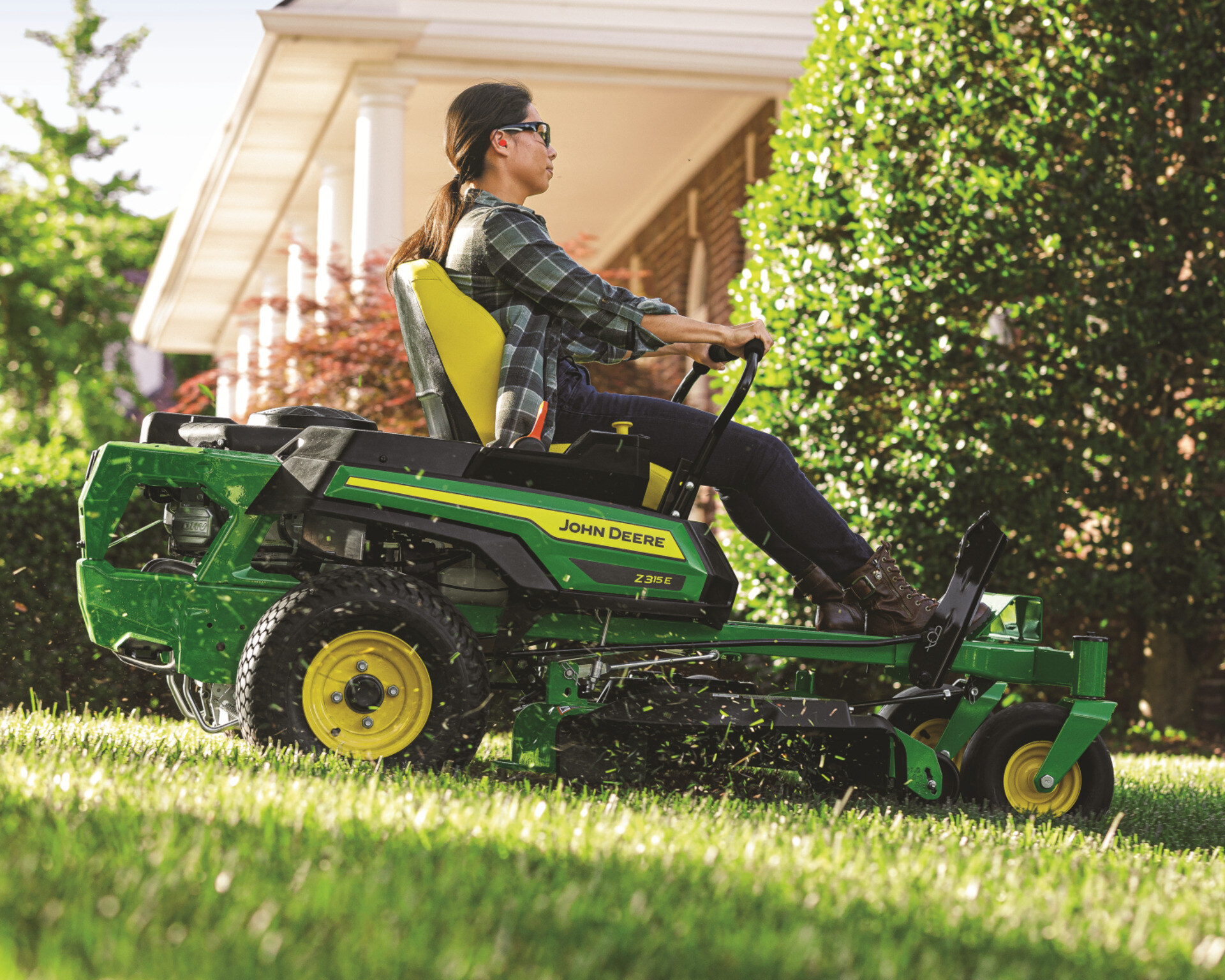 A worker mows a lawn with a John Deere Z315E zero-turn mower.