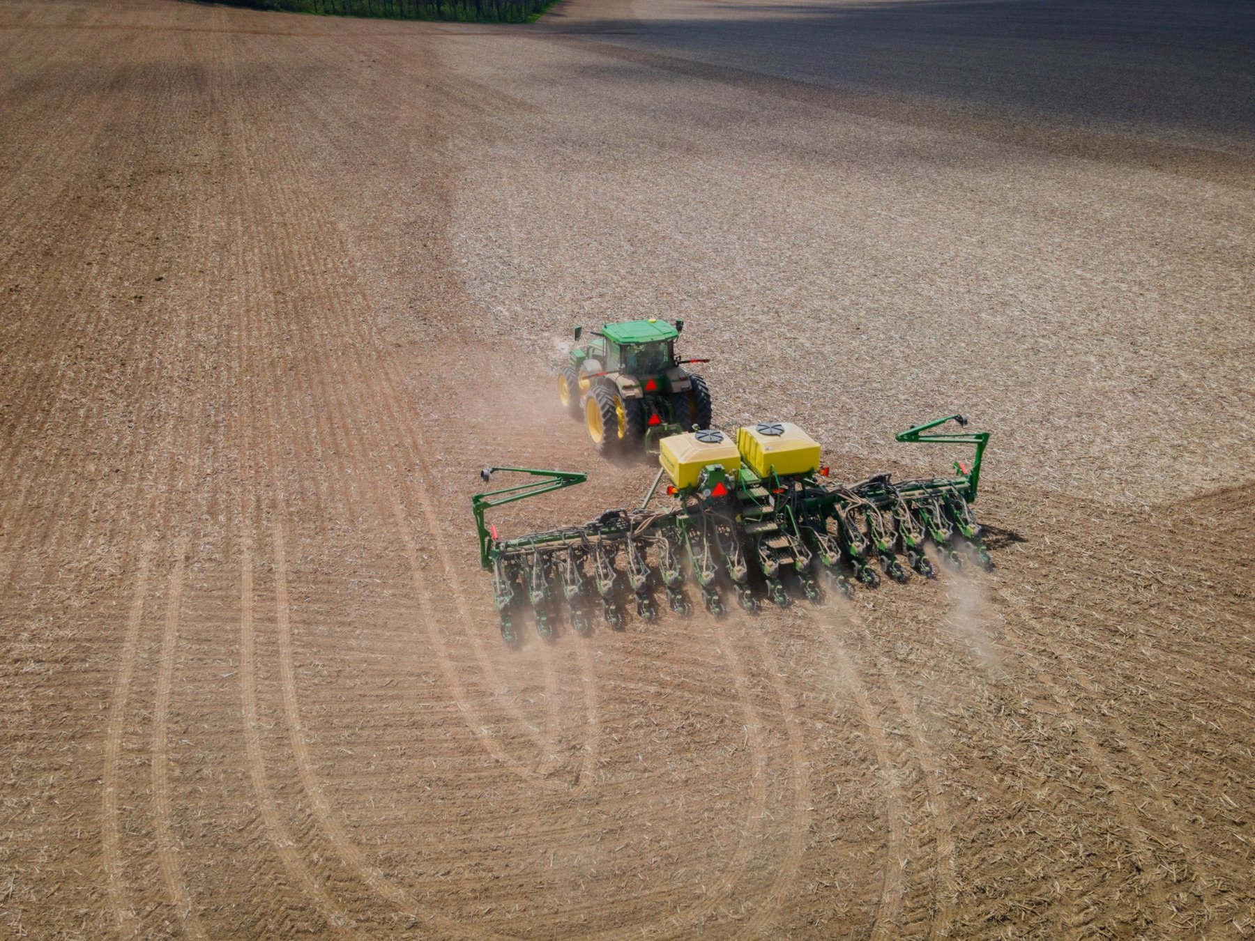 Aerial view of a John Deere tractor with a StarFire receiver pulling a planter across a spring field.