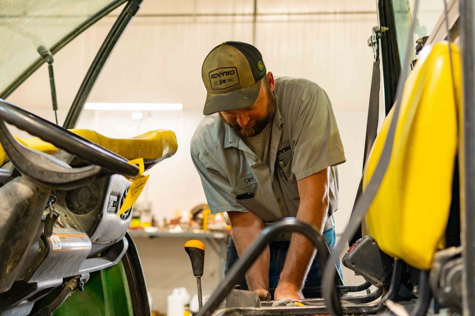 A Koenig technician works on the rear hitch of a John Deere compact tractor in a dealership shop.