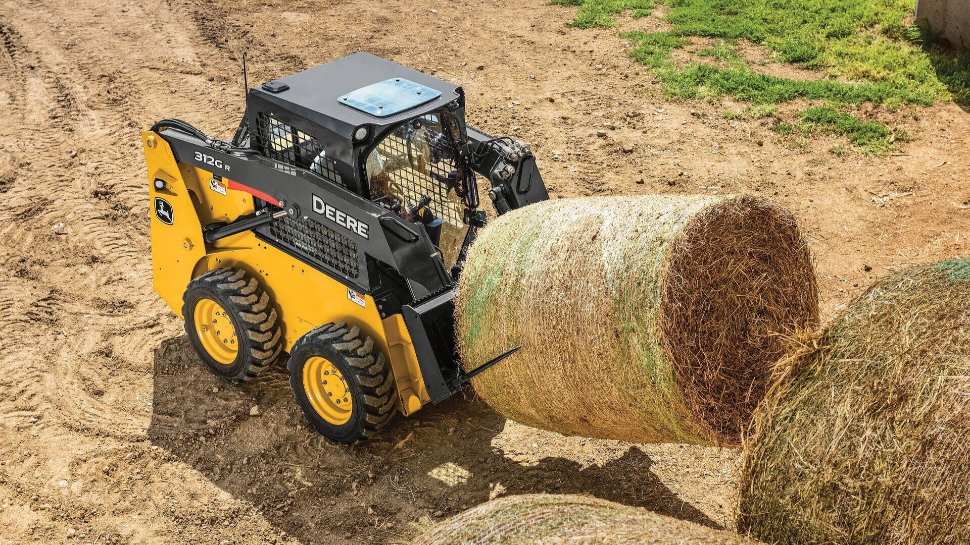 312G Skid Steer moving large hay bale on a farm